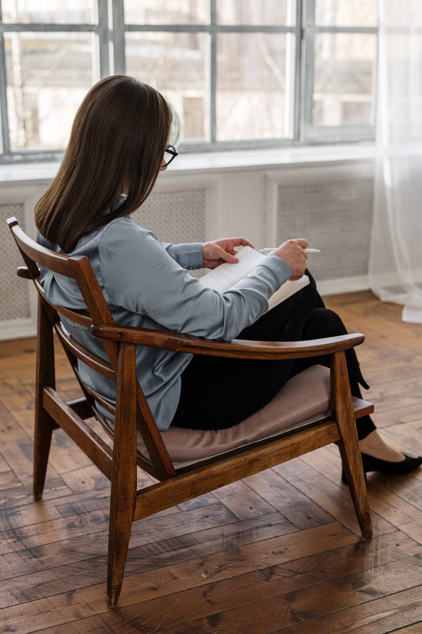 Kobieta w koszuli z długim rękawem siedząca na brązowym drewnianym krześle.